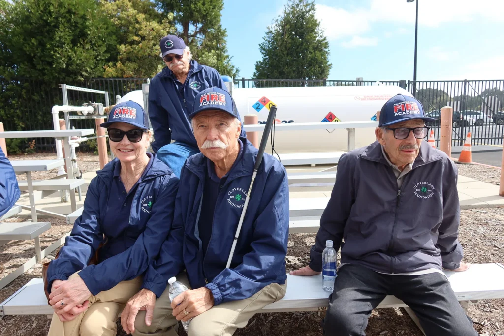 Cloverlane Foundation members in Fire Academy caps seated on bleachers