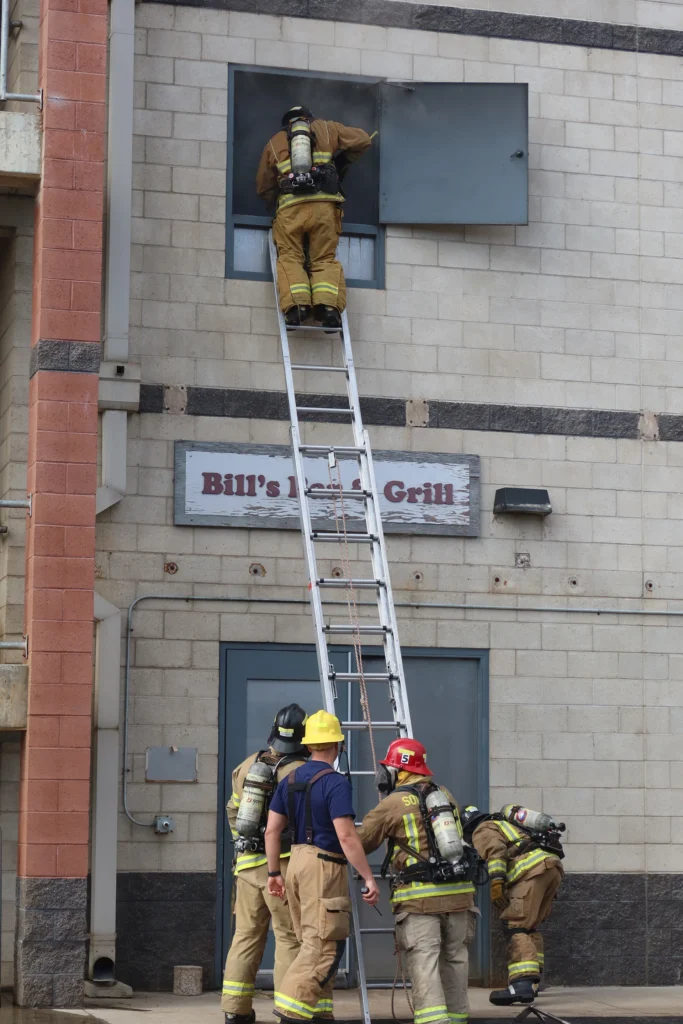 Fire academy recruit climbing a ladder into a window during a drill