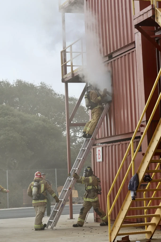 Firefighter climbing down a ladder from a smoky training tower window