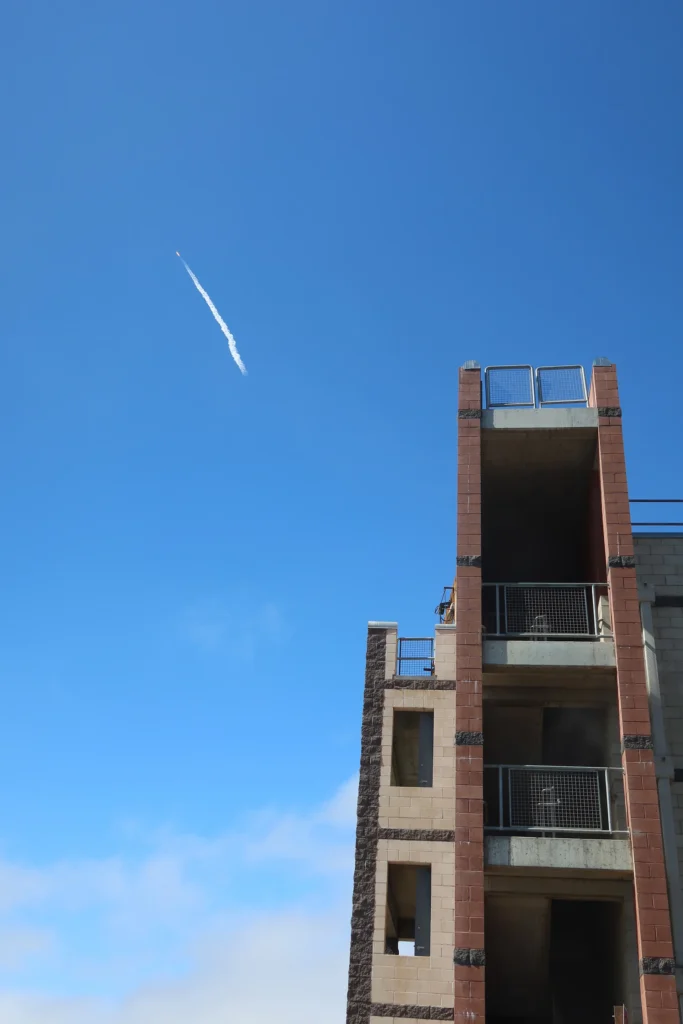 Rocket contrail in blue sky above a fire training tower